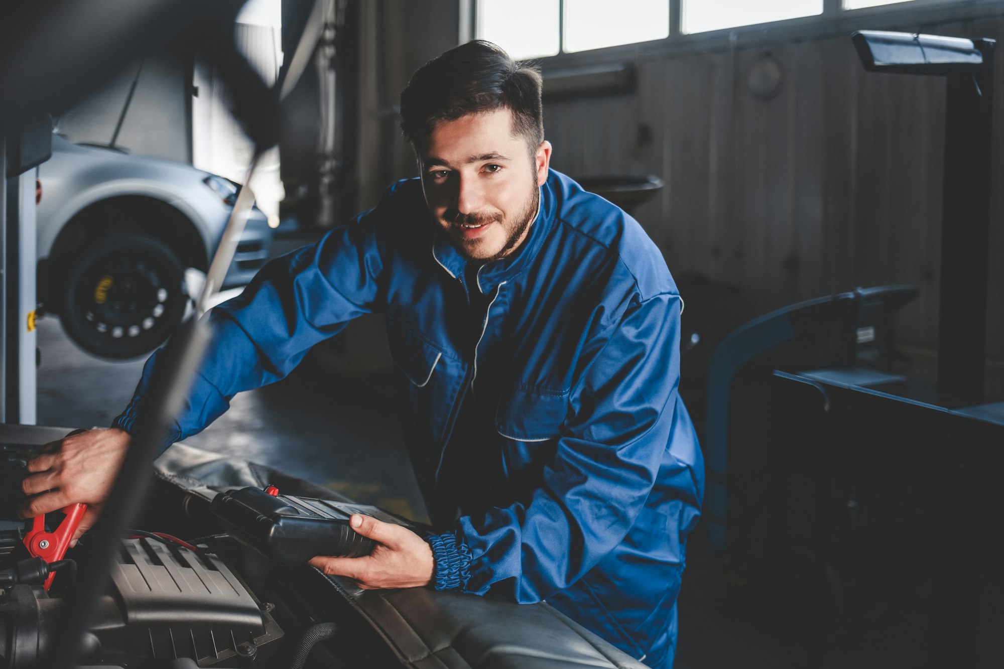 Auto mechanic with a electric device checks the condition of the car battery